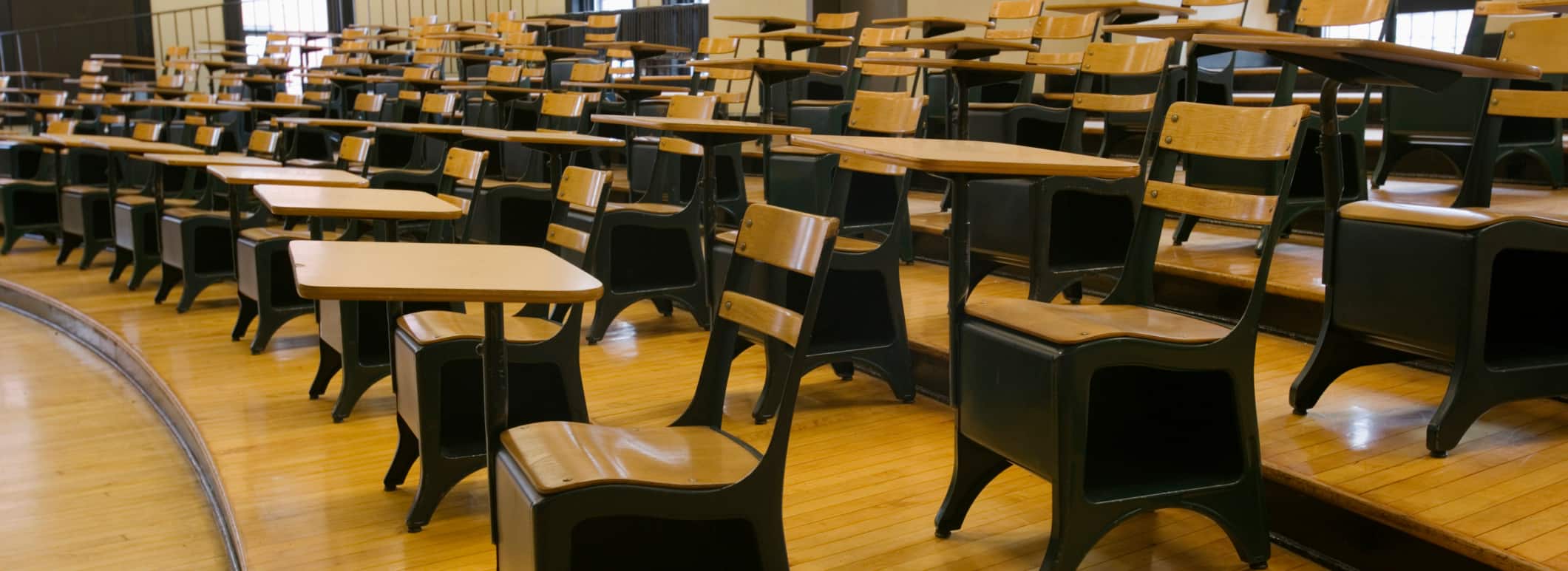 Empty college classroom with black and tan chairs on polished wooden tiers.