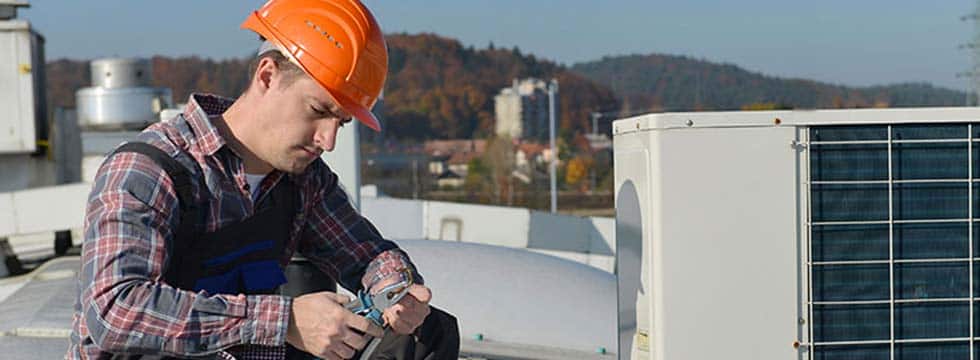 A technician completing HVAC service on a rooftop uses pliers on a wire.