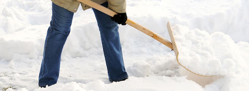 A blue-jeaned person shovels a path in deep snow.