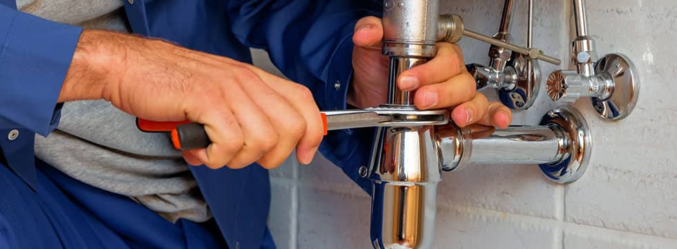 A professional plumber tightens fittings under a sink. 