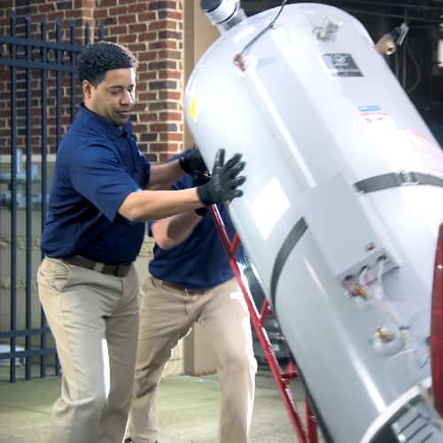 Two Ferguson associates push a commercial water heater on a dolly outside of a building.