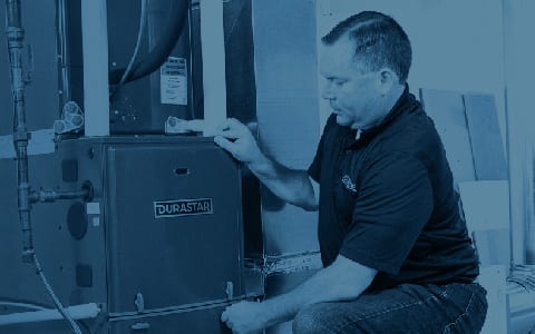 An HVAC technician kneels and places his hands on a Durastar furnace panel.