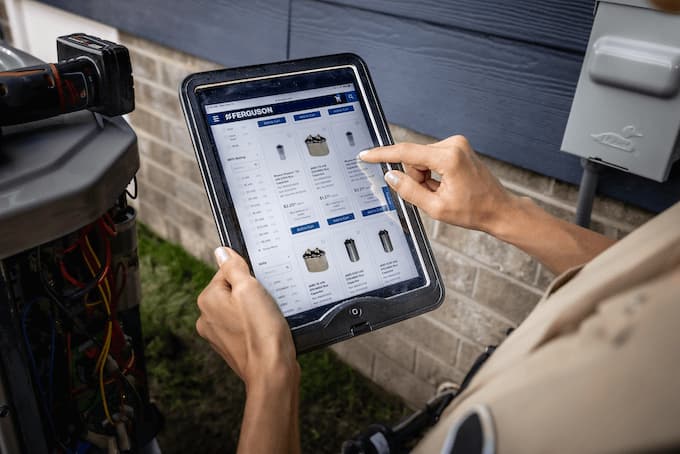 An HVAC contractor swipes through the Ferguson app on her tablet while working on an HVAC unit outside.