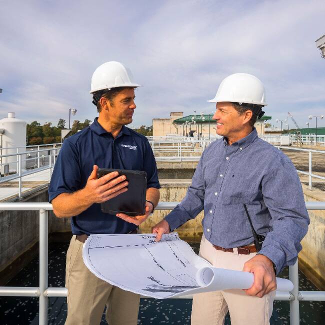 A Ferguson associate holding a large tablet discusses a shop drawing with a contractor outside at a water treatment plant.