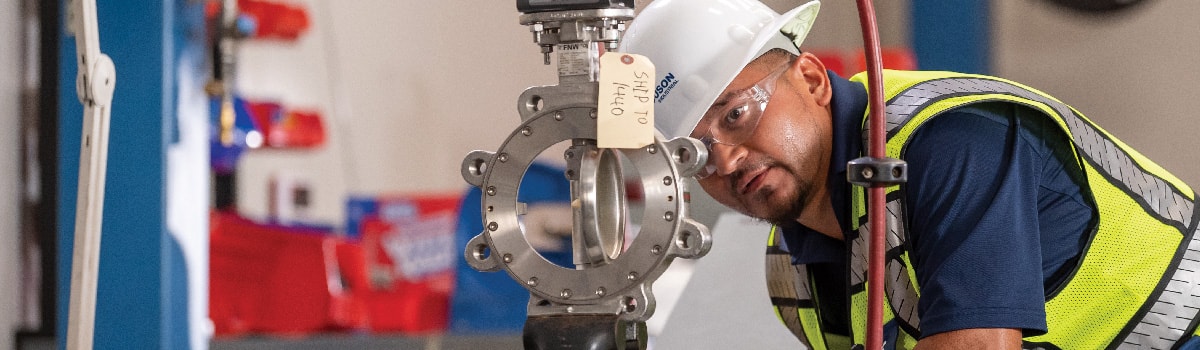 A Ferguson associate wearing a hard hat and reflective vest examines a butterfly valve ready with a shipping tag attached to it.