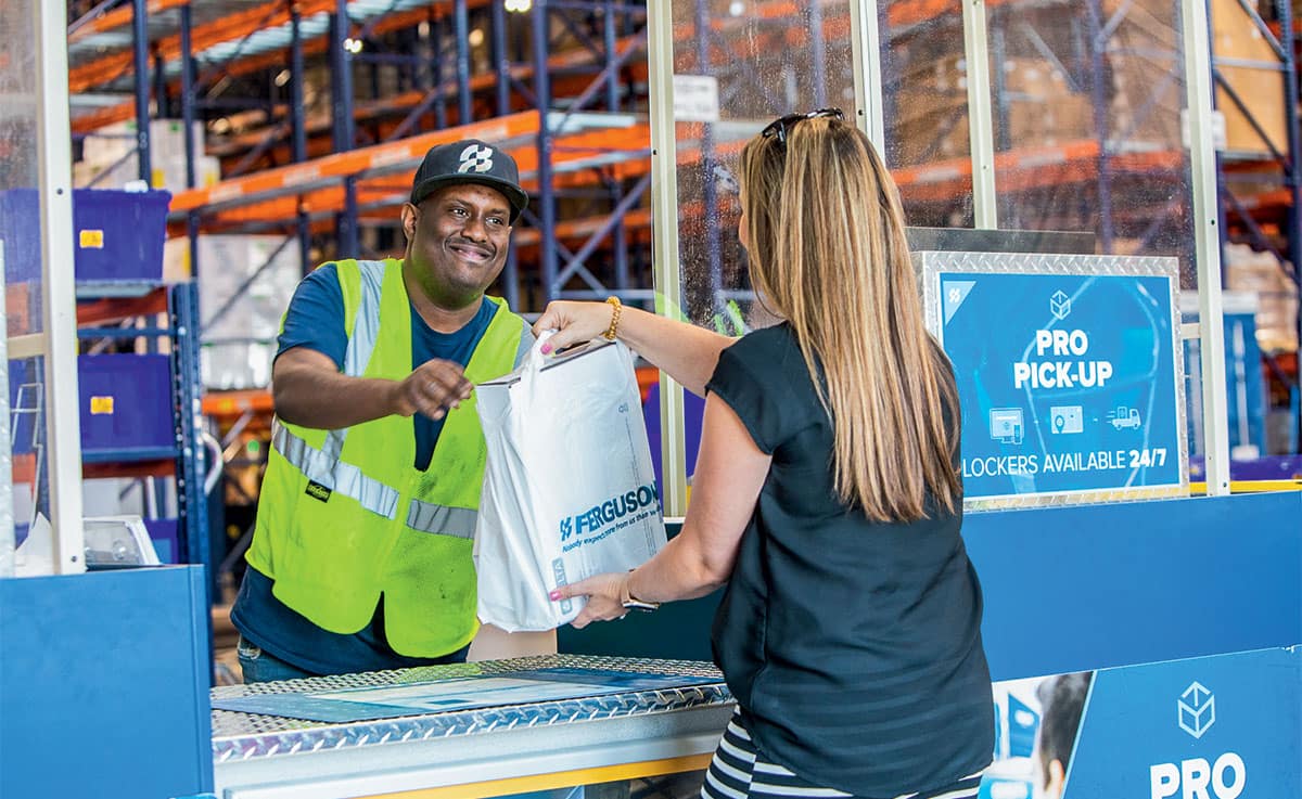 At a Pro Pick-Up location, a smiling Ferguson associate hands a Ferguson bag of supplies to a contractor.