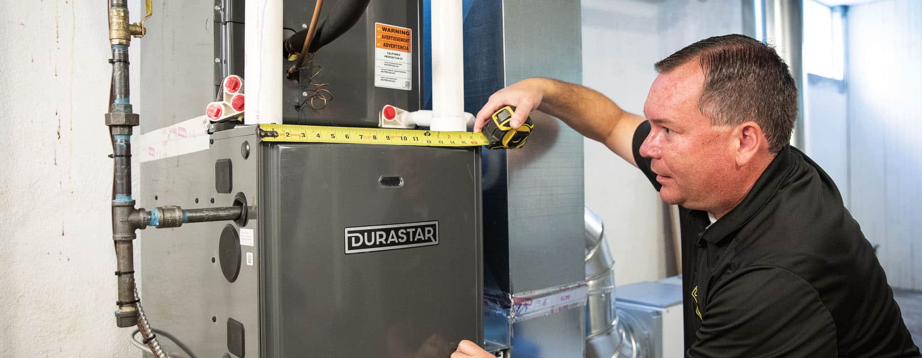 An HVAC technician holds a measuring tape horizontally across a Durastar furnace panel.