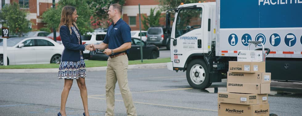 A Ferguson associate shakes hands with a multifamily property manager in an apartment complex parking lot. A Ferguson truck and packages on a dolly are in the background.