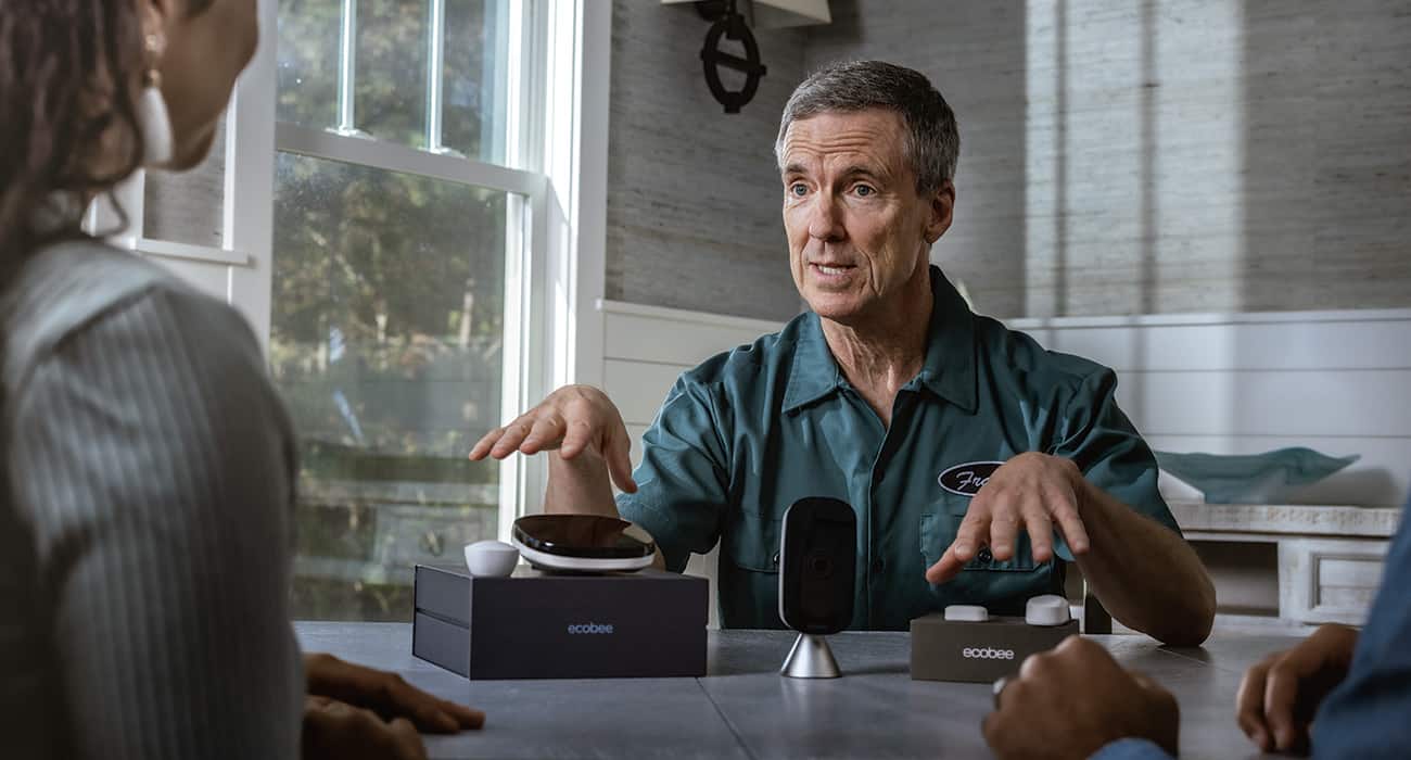 An HVAC contractor discusses an ecobee smart thermostat with two customers at their kitchen table.