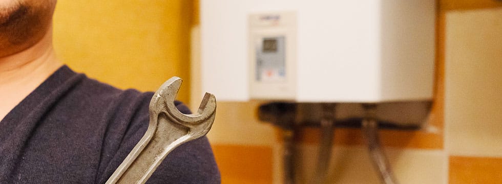 A contractor holds a wrench in front of a wall-mounted tankless water heater.
