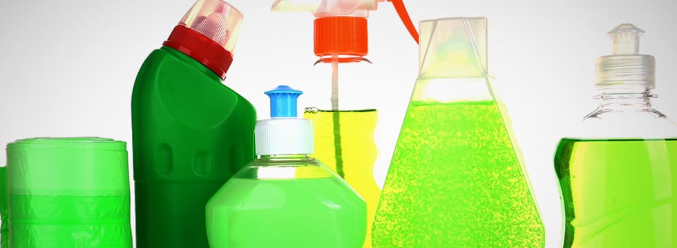 A collection of green and clear bottles containing green cleaning solution in front of a white background.