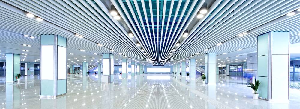 An ultra-modern office building lobby in cool blue and white tones, lit with LED columns and overhead LED lighting, which reflects off the highly polished floor.
